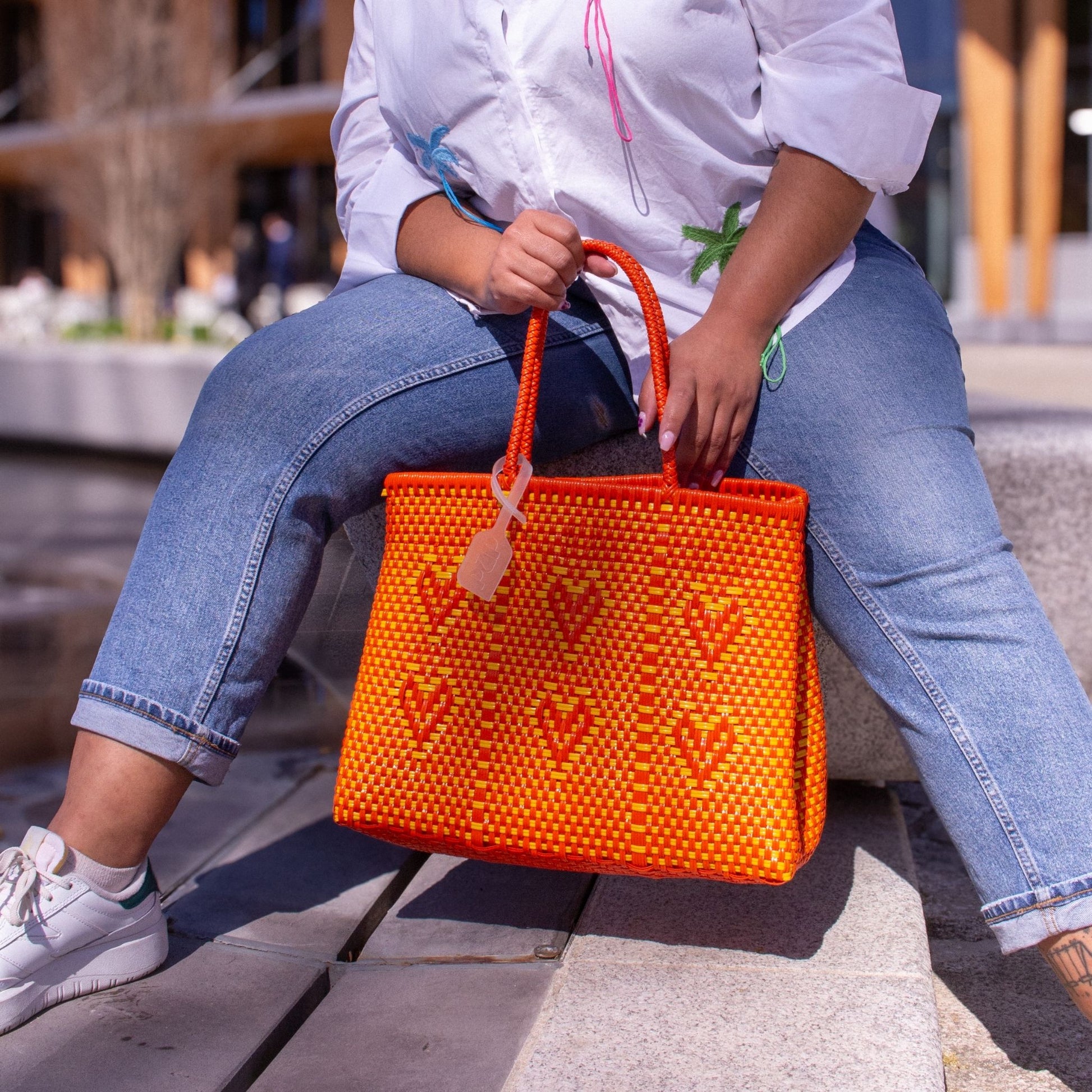 Madie illumine sa tenue avec le sac Chéri M Capucine, aux couleurs orange et jaune, tressé en plastique recyclé avec des cœurs.