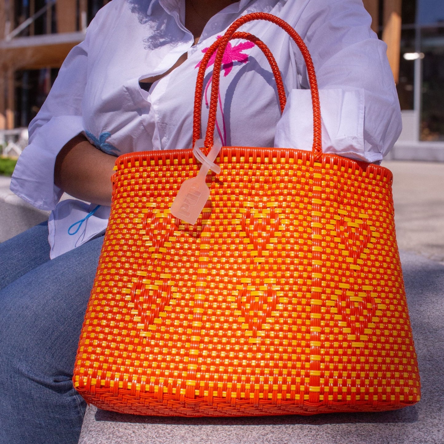 Plan rapproché du sac Chéri M Capucine, dévoilant ses cœurs tressés et son duo de couleurs orange et jaune.