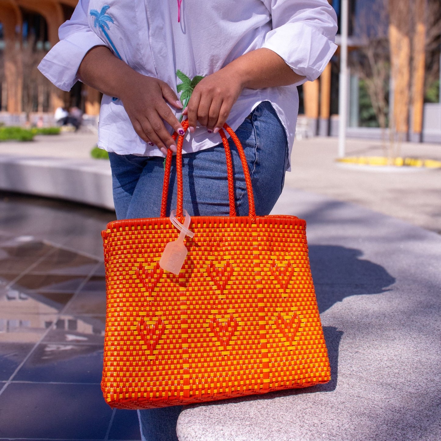 Le sac Chéri M Capucine, orange et jaune, tressé en plastique recyclé, porté par Madie, au style ensoleillé.