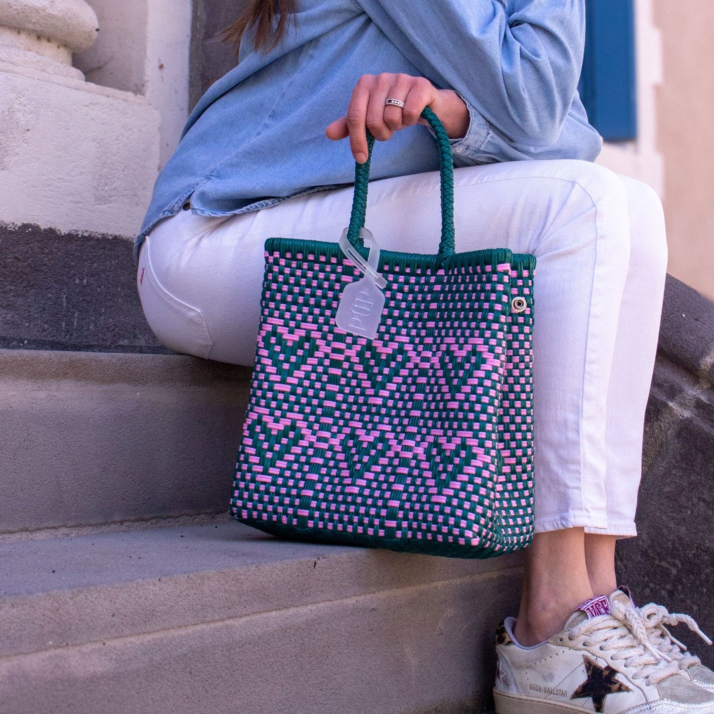 Le sac Chéri S Calista, vert et rose, tressé avec des cœurs en plastique recyclé, posé à côté d'Anna.