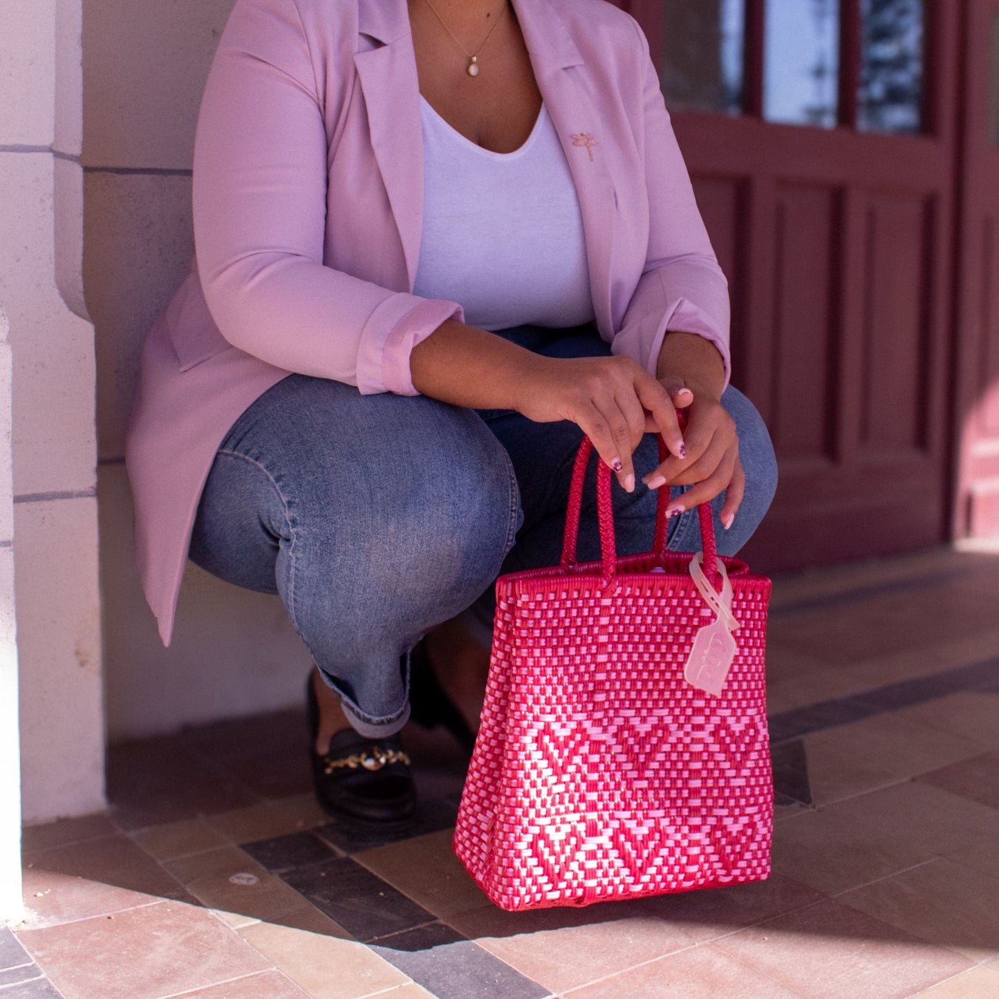 Madie porte le sac Chéri S Camélia, bicolore rose et rouge, tressé en plastique recyclé avec un motif cœurs.