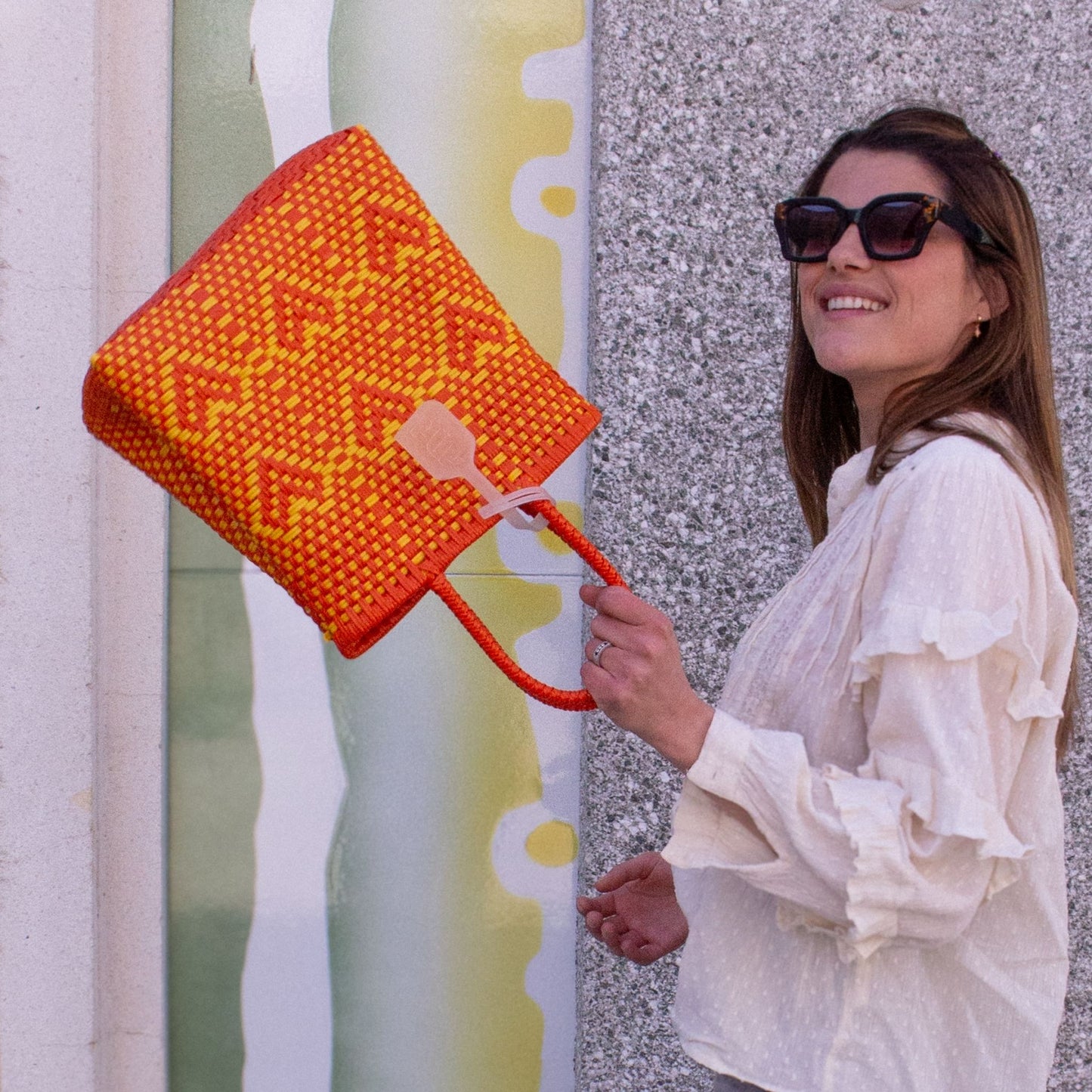 Le sac Chéri S Capucine, orange et jaune, orné de cœurs en plastique recyclé, porté avec gaieté par Anna.
