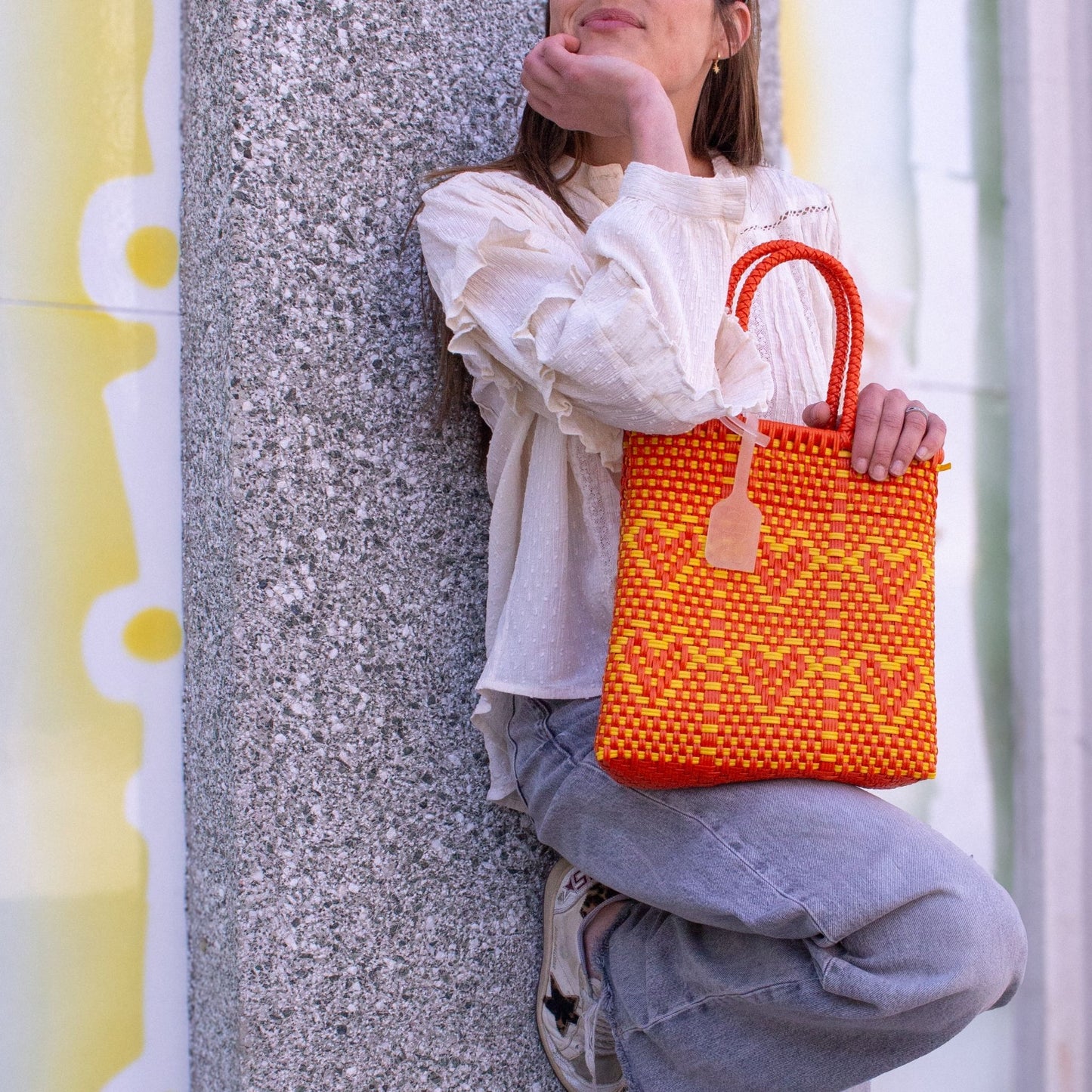 Anna porte le sac Chéri S Capucine, tressé en plastique recyclé, bicolore orange et jaune, motif cœurs.