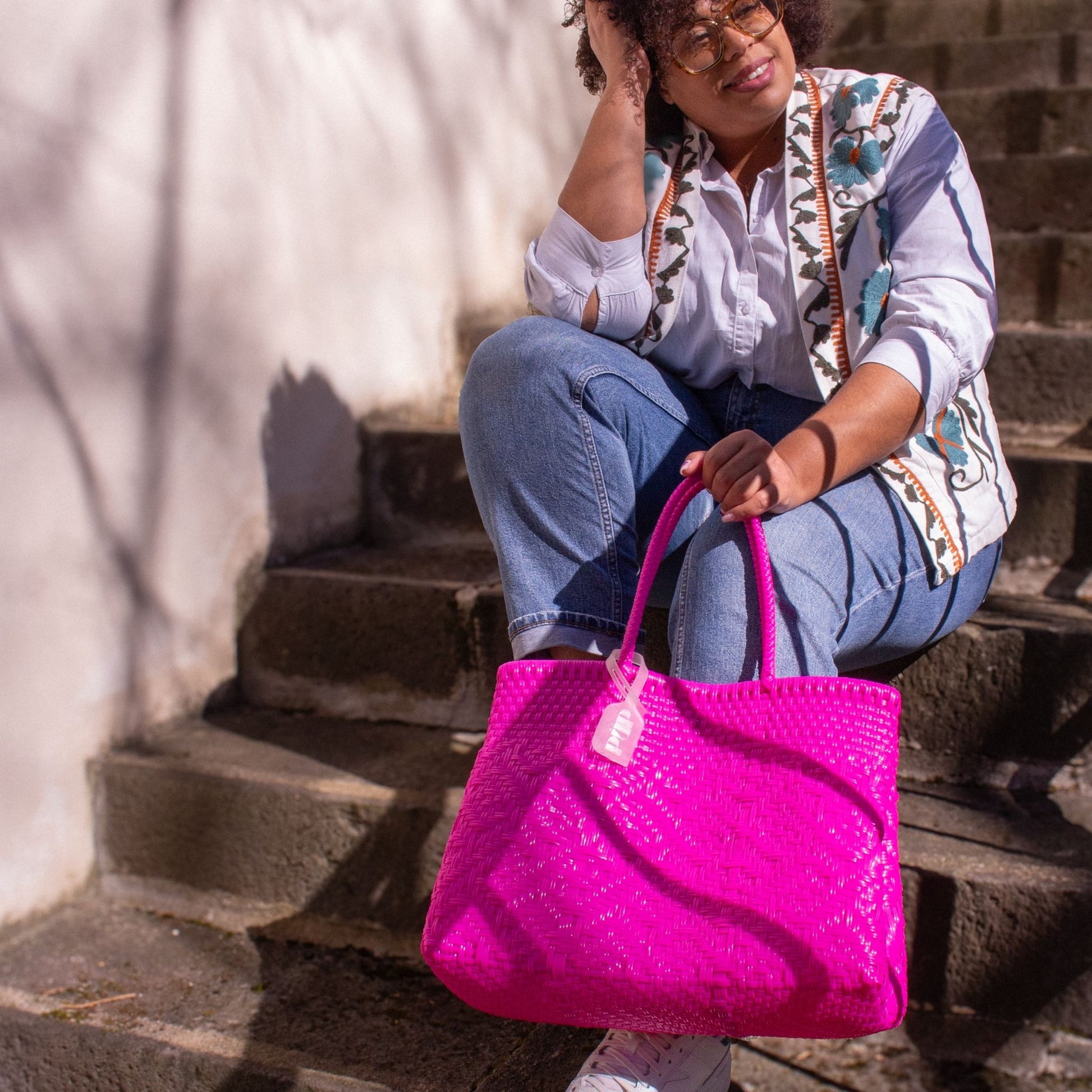 Madie porte le sac Loom M Bougainvillier, au tressage rose en plastique recyclé.