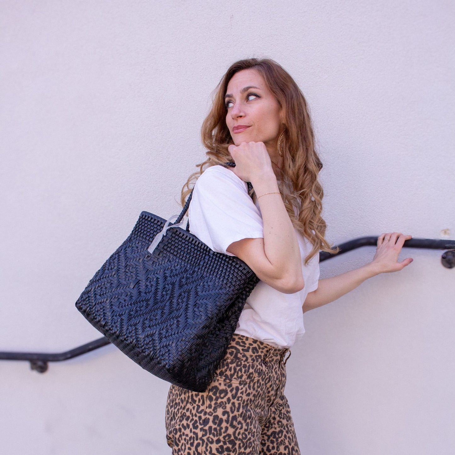 Emmanuelle accessoirise sa tenue avec le sac Loom M Charbon, noir et tressé en plastique recyclé.