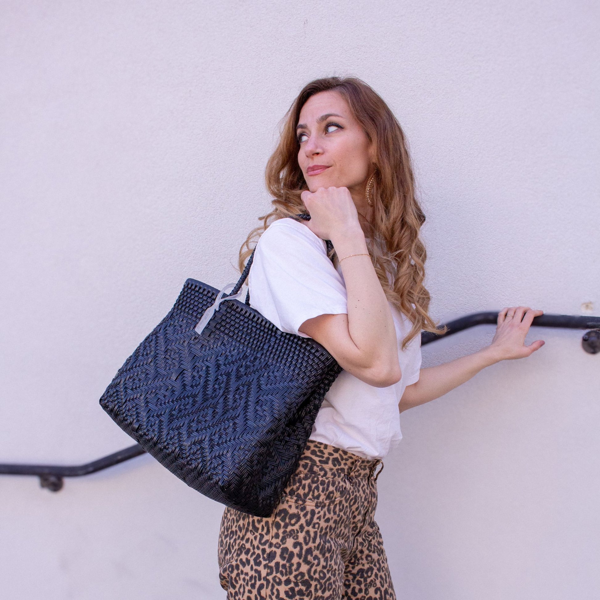 Emmanuelle accessoirise sa tenue avec le sac Loom M Charbon, noir et tressé en plastique recyclé.