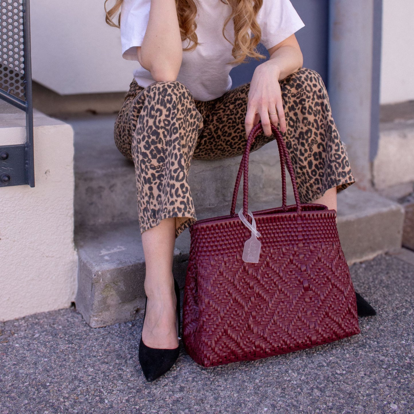 Le sac Loom M Lie de Vin, tressé en plastique recyclé, porté par Emmanuelle au style affirmé.