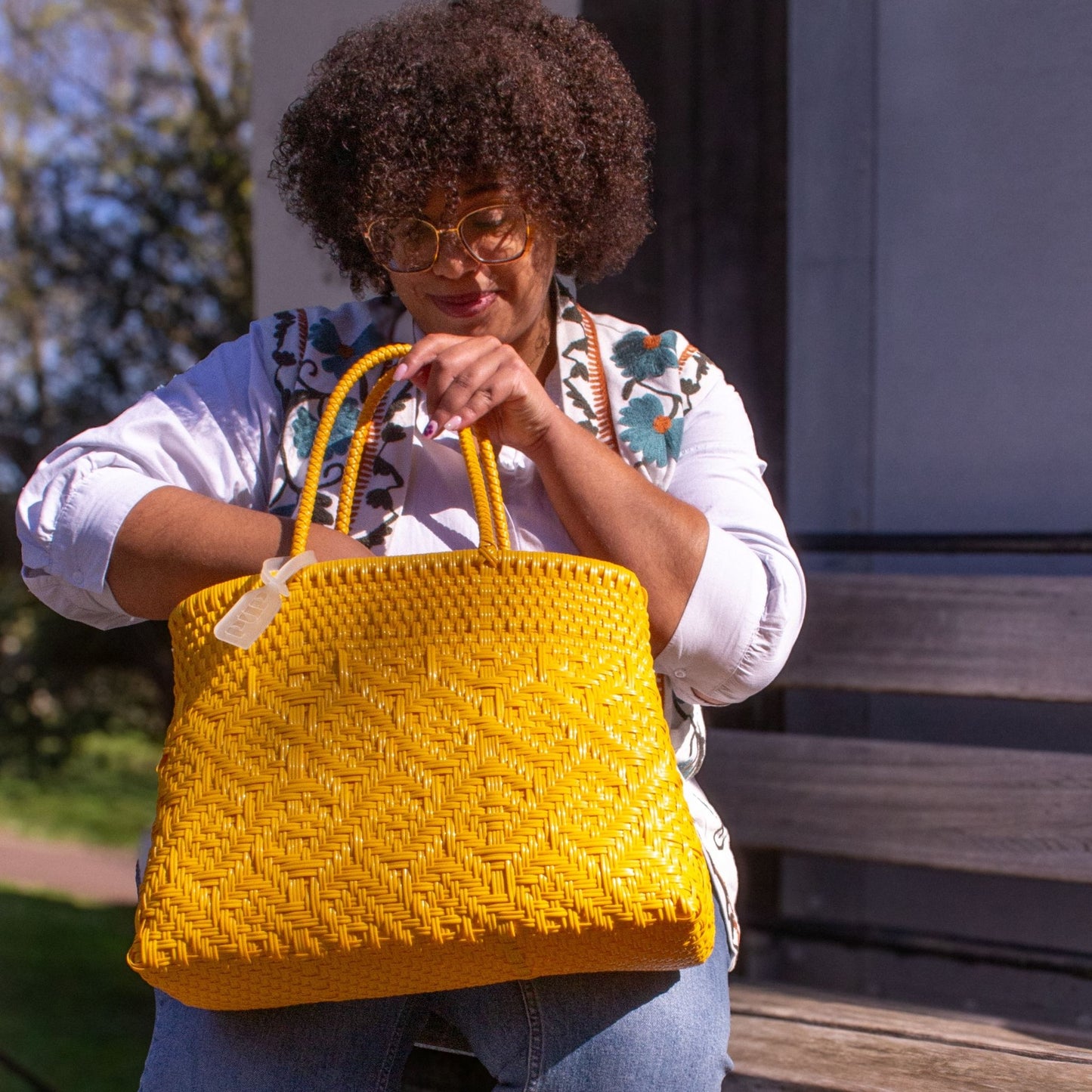 Madie accessoirise sa tenue avec le sac Loom M Mangue, tressé en plastique recyclé, coloris jaune.