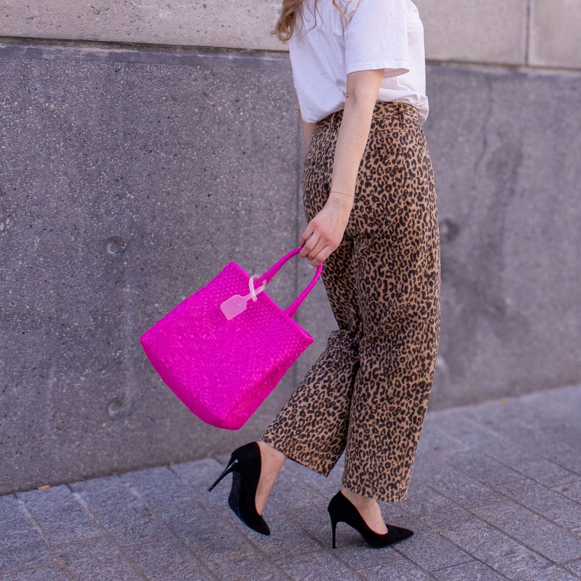 Emmanuelle porte le sac Loom S Bougainvillier, tressé en plastique recyclé, dans une teinte rose éclatante.