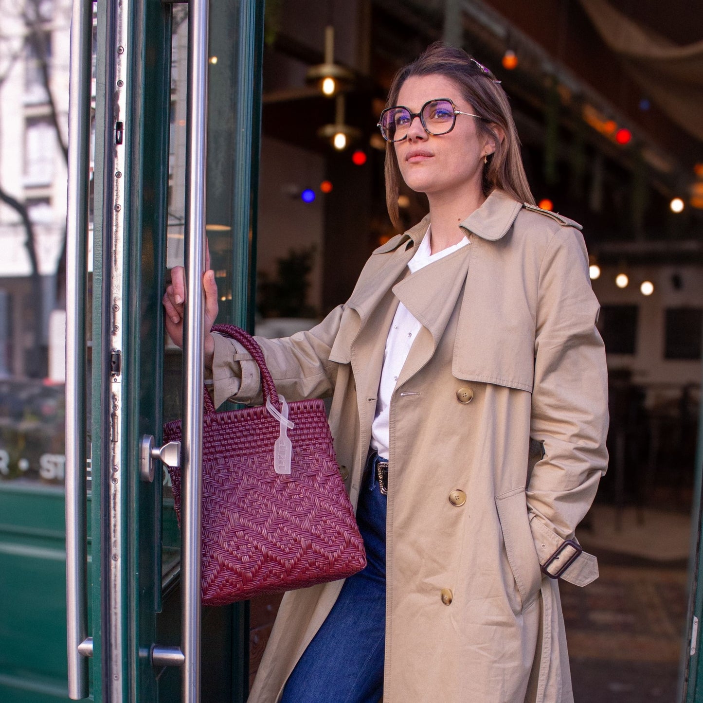 Anna porte le sac Loom S Lie de Vin, tressé en plastique recyclé, dans une élégante nuance bordeaux.