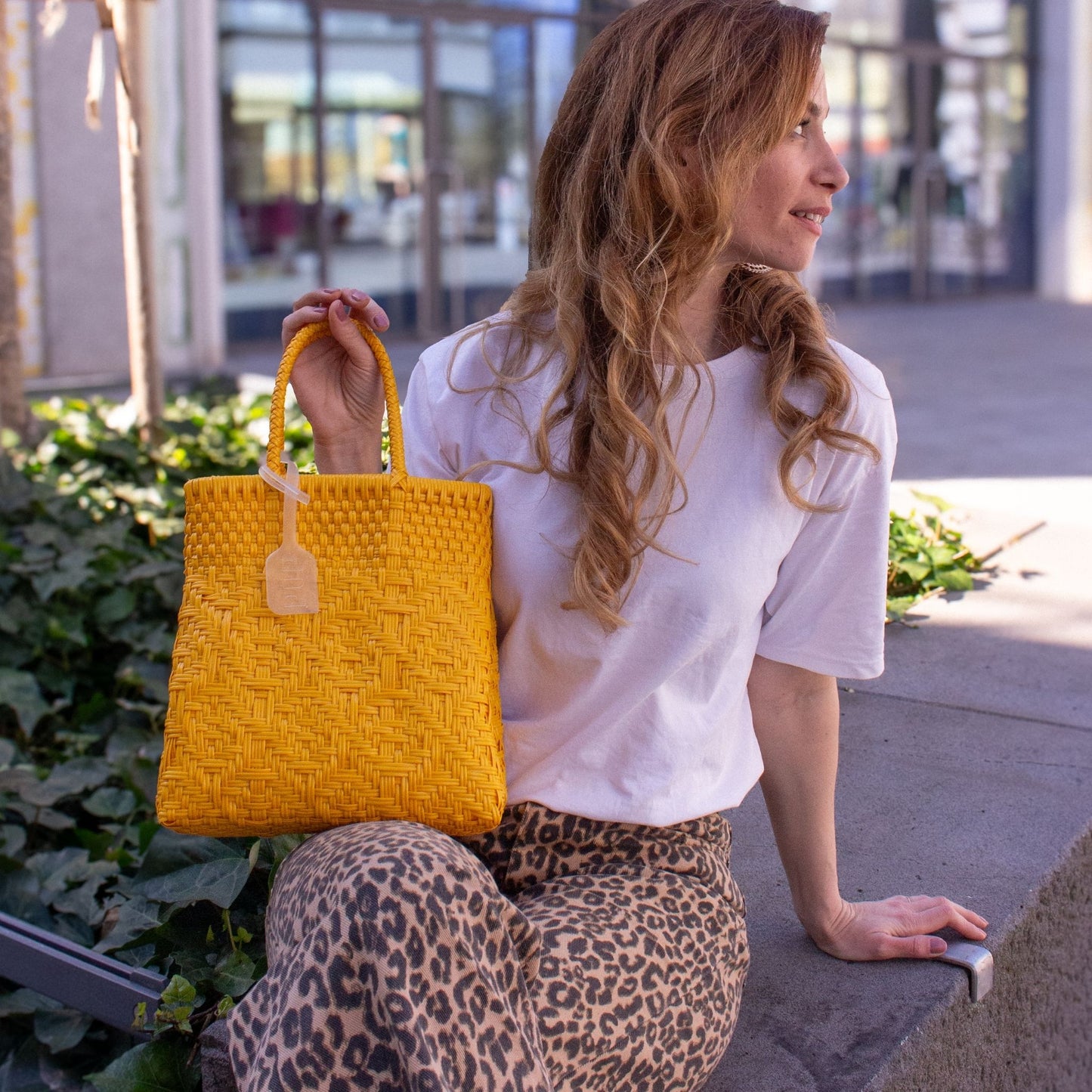 Emmanuelle porte le sac Loom S Mangue, tressé en plastique recyclé, dans un jaune lumineux.