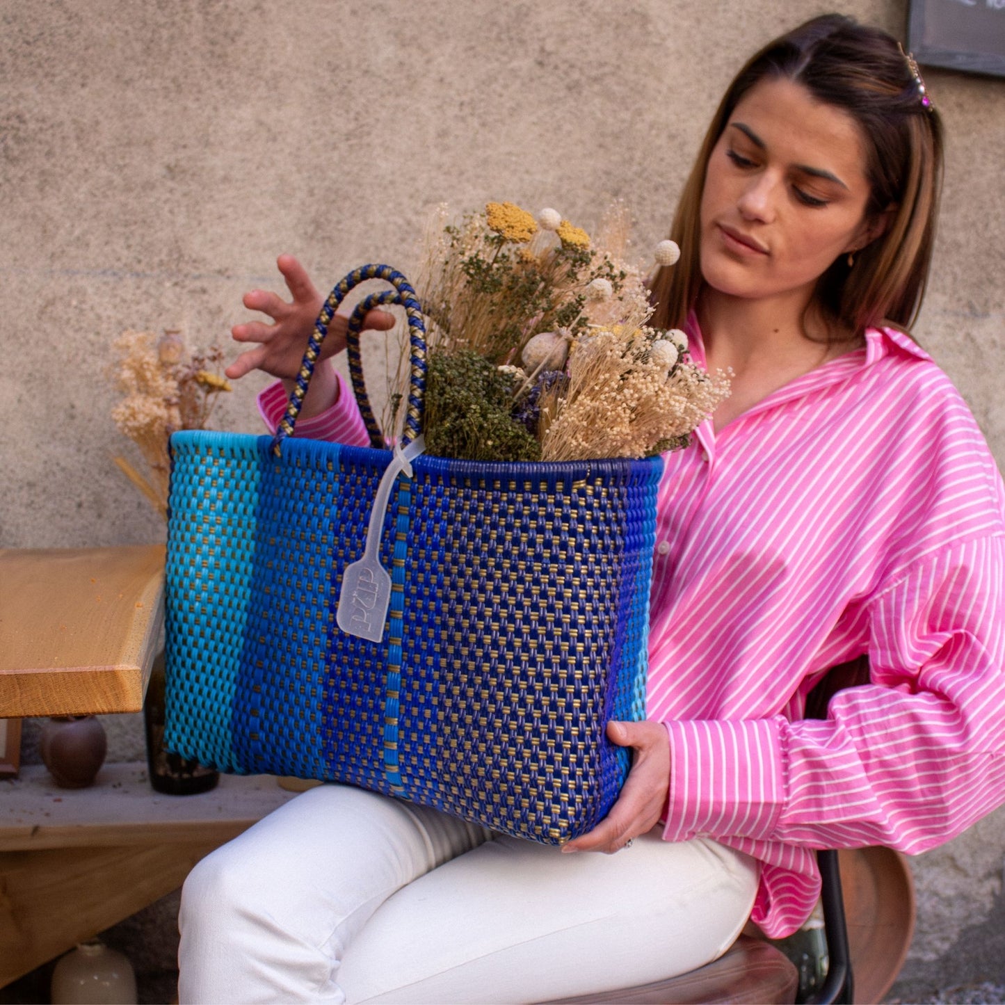 Anna tient le panier Medium Nox sur ses genoux, design sobre et élégant en plastique tressé bleu.