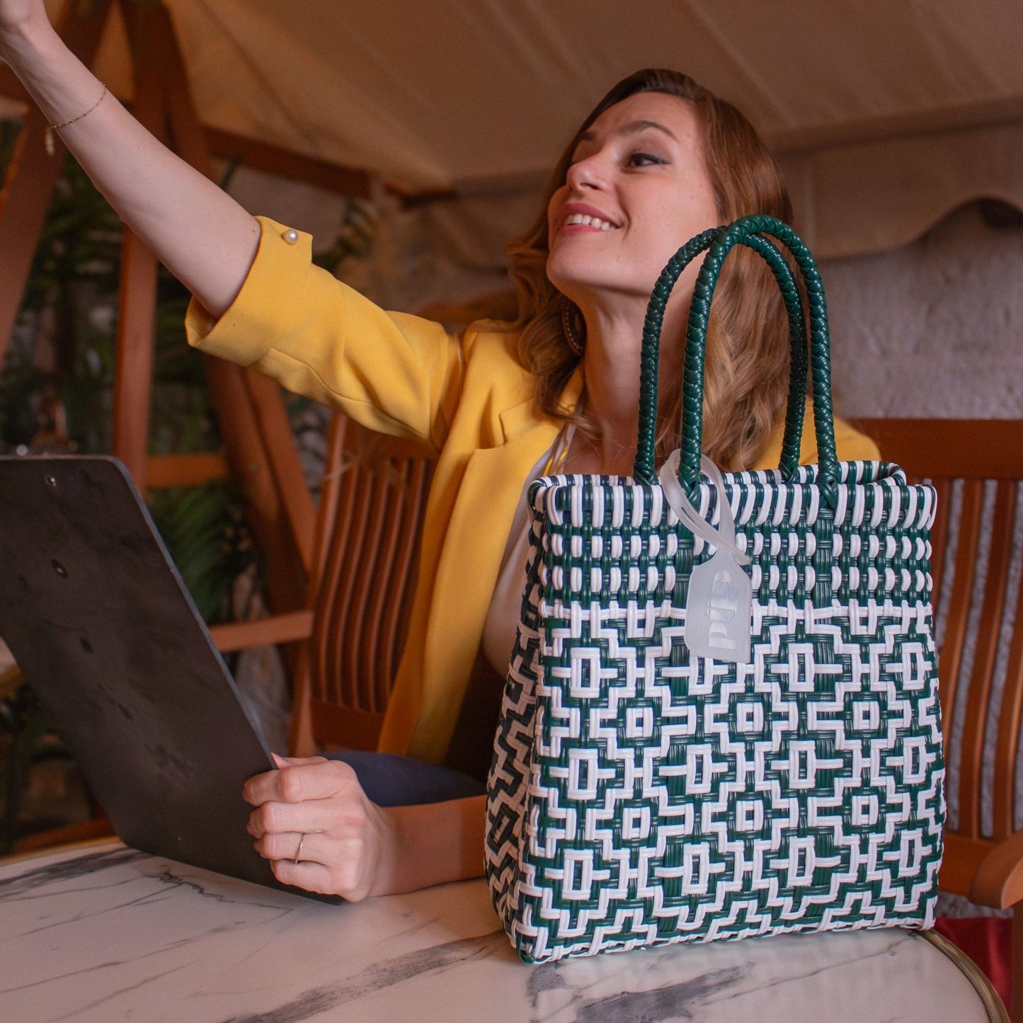 Le sac Mosaïc S Jade, blanc et vert, posé à côté d'Emmanuelle qui travaille au café.