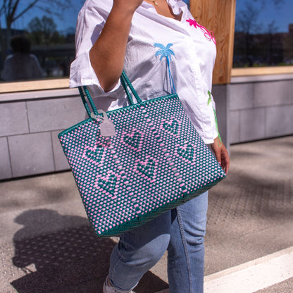 Madie affiche le sac Chéri M Calista, aux nuances vert et rose, tressé en plastique recyclé et décoré de cœurs.