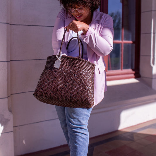 Madie porte le sac Loom M Chocolat, tressé en plastique recyclé, teinte marron chaleureuse.