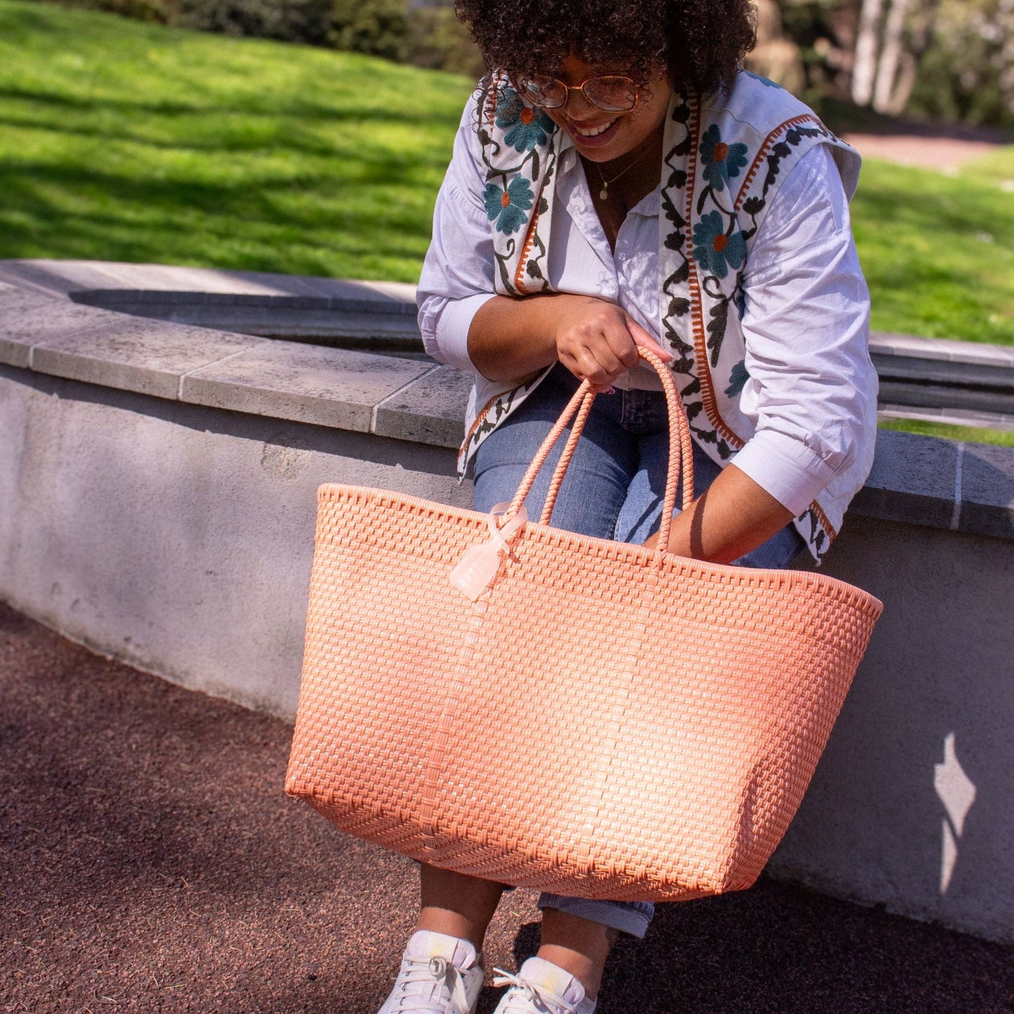 Madie regarde à l'intérieur de son panier Maxi Saumon au tressage en plastique recyclé de couleur rose.