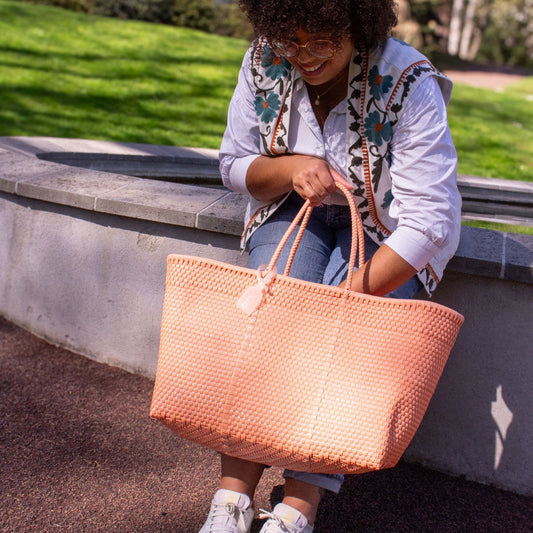 Madie regarde à l'intérieur de son panier Maxi Saumon au tressage en plastique recyclé de couleur rose.