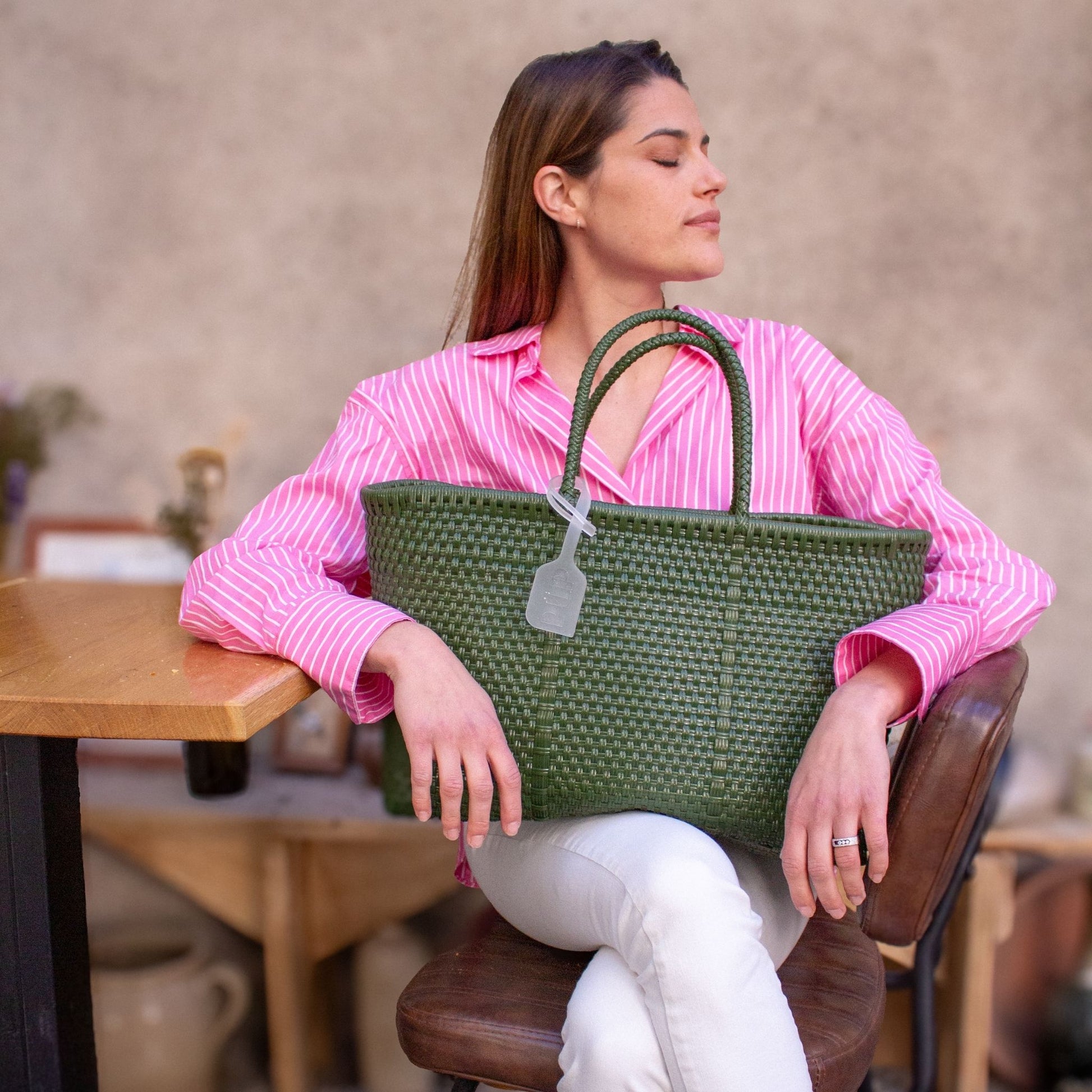 Anna est assise et porte sur ses genoux le panier Medium Olive tressé en plastique recyclé de couleur verte.
