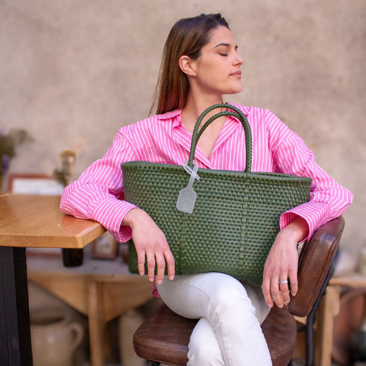Anna est assise et porte sur ses genoux le panier Medium Olive tressé en plastique recyclé de couleur verte.