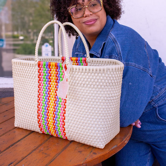 Le panier Medium Pastel est posé sur une table en terrasse aux côtés de Madie. Tressé en plastique recyclé multicolore.