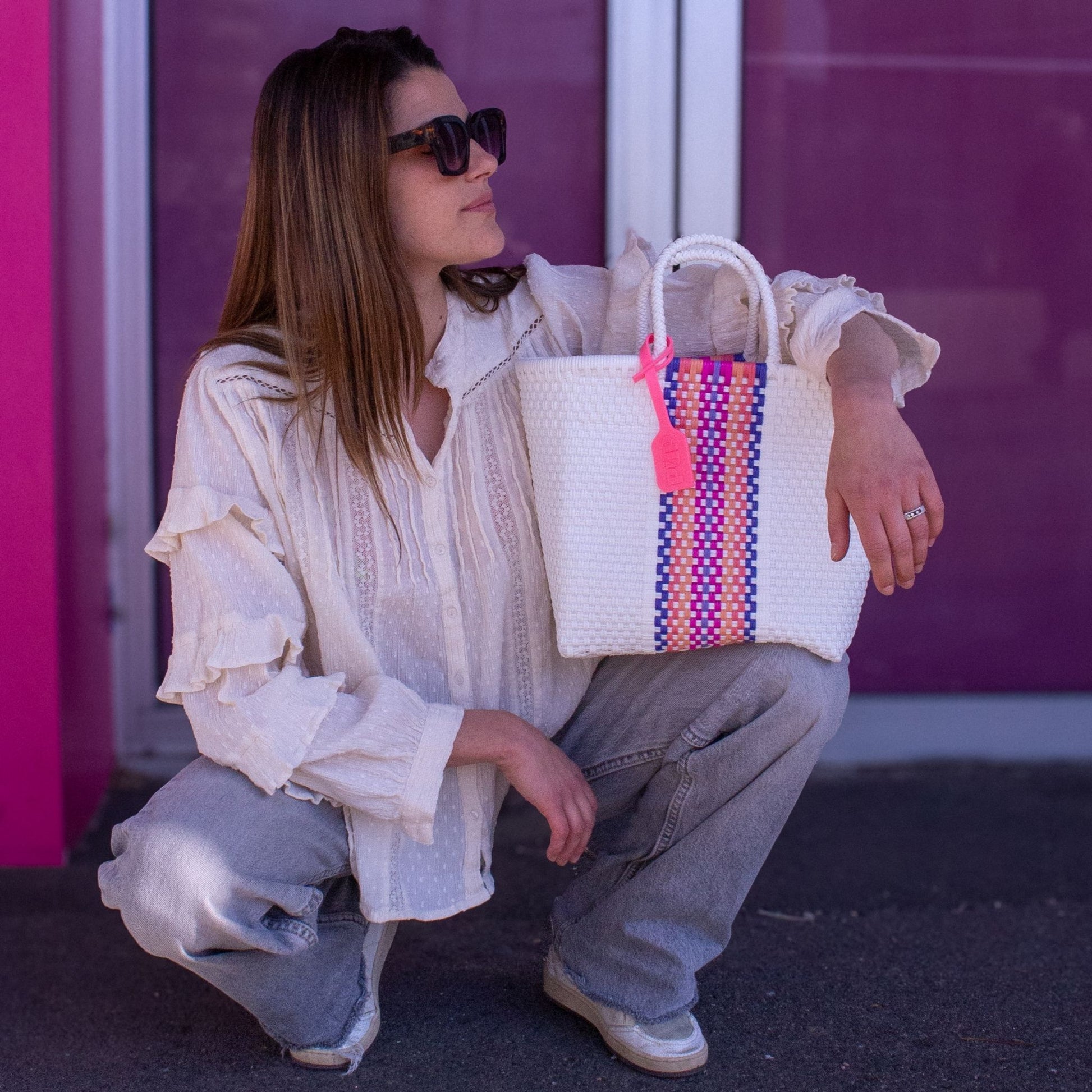 Anna fait reposer son panier Small  Orchidée sur ses genoux. En plastique recyclé blanc avec bande colorée.